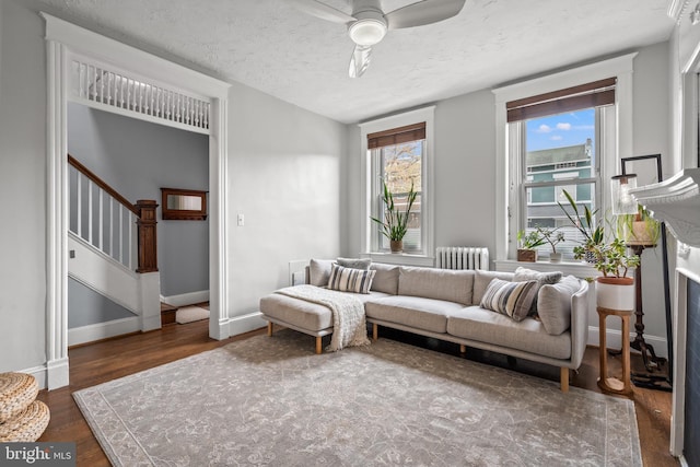 living area featuring radiator, a ceiling fan, wood finished floors, stairs, and baseboards