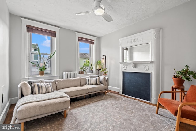 living room with ceiling fan, a fireplace, a textured ceiling, radiator heating unit, and baseboards