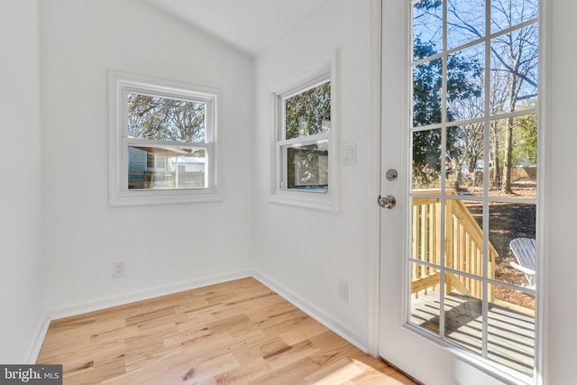 doorway to outside featuring baseboards, light wood finished floors, and vaulted ceiling