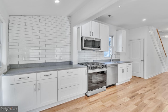 kitchen with light wood-style flooring, a sink, stainless steel appliances, white cabinets, and tasteful backsplash