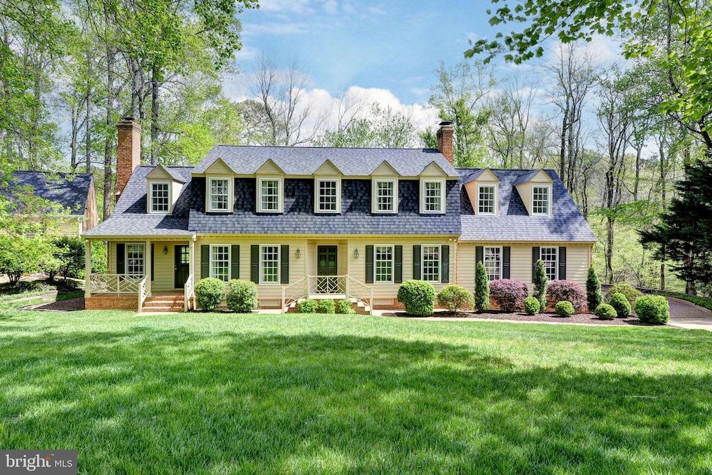 cape cod-style house featuring a front yard, roof with shingles, and a chimney
