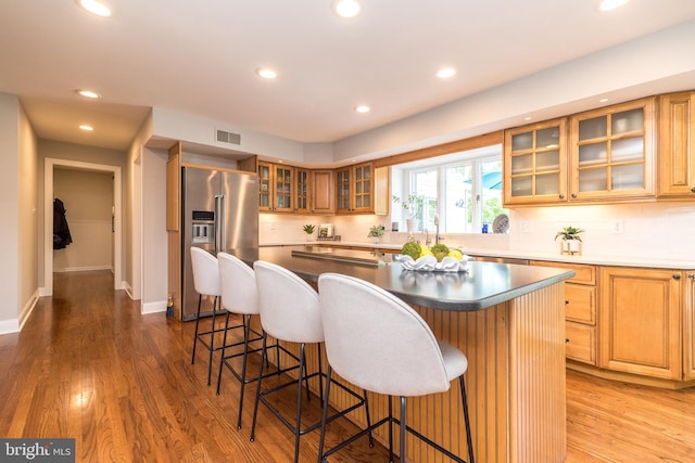 kitchen featuring high end fridge, a kitchen island, tasteful backsplash, recessed lighting, and glass insert cabinets