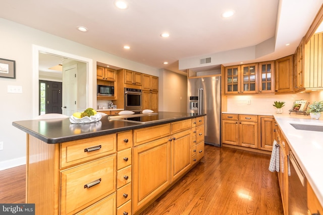 kitchen with appliances with stainless steel finishes, dark wood finished floors, recessed lighting, a center island, and glass insert cabinets