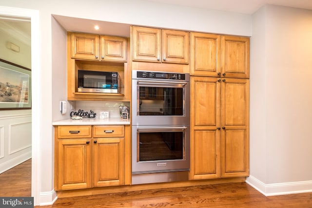 kitchen with appliances with stainless steel finishes, wood finished floors, a warming drawer, and light countertops