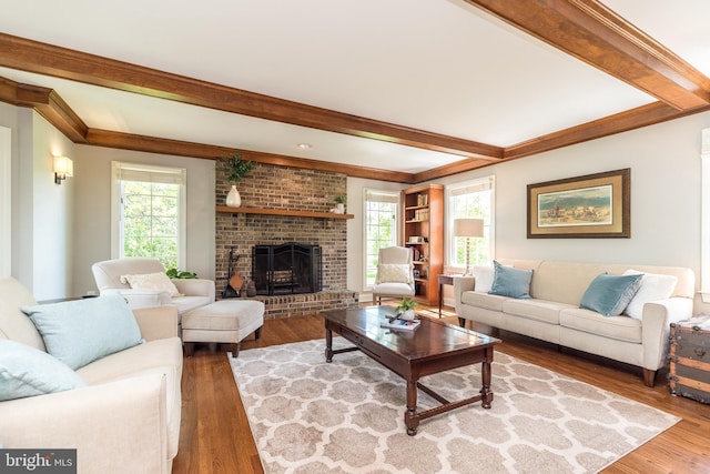 living area with wood finished floors, beamed ceiling, a brick fireplace, and plenty of natural light