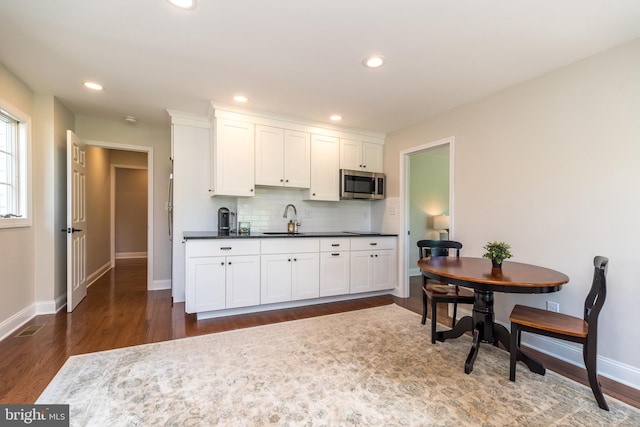kitchen featuring stainless steel microwave, a sink, dark wood finished floors, dark countertops, and decorative backsplash