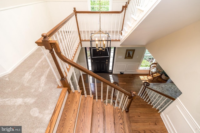 stairway featuring a decorative wall, a chandelier, wood finished floors, and a wainscoted wall