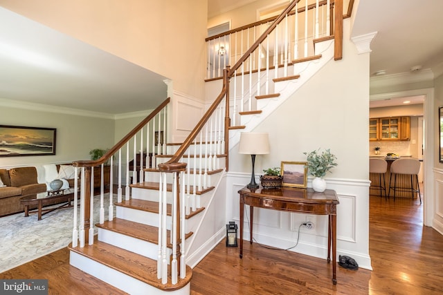 stairway with ornamental molding, wood finished floors, a wainscoted wall, and a decorative wall