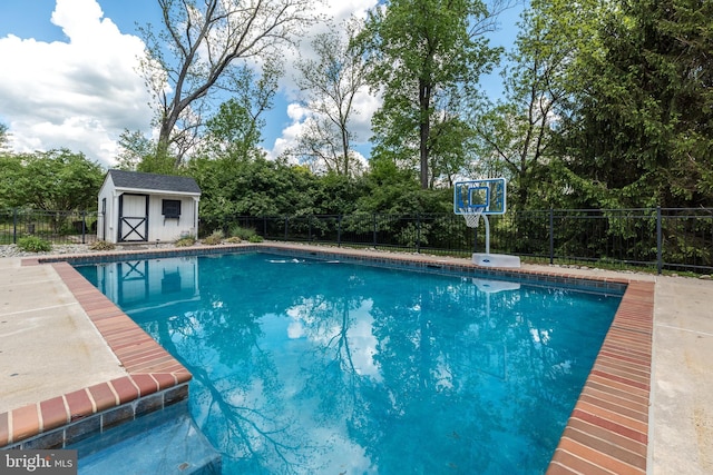 view of pool featuring fence, a shed, view of scattered trees, and an outbuilding