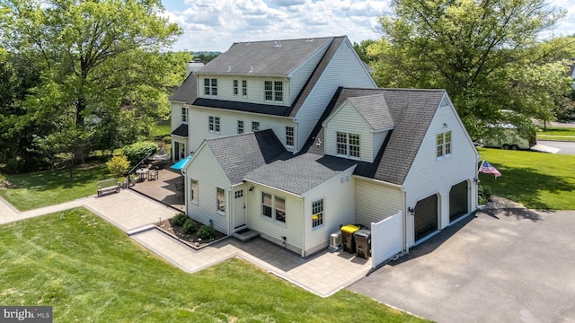 back of property with an attached garage, asphalt driveway, a patio, roof with shingles, and a yard