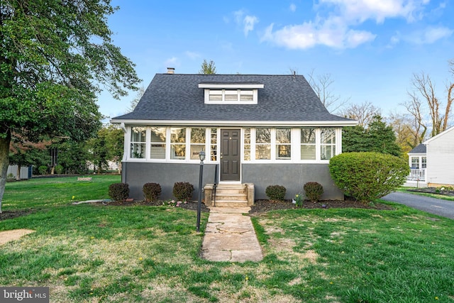 bungalow-style home with a shingled roof, entry steps, a chimney, and a front lawn