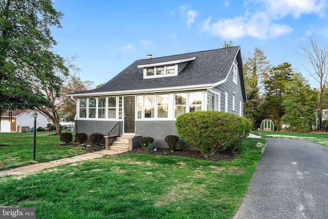 bungalow-style home with stucco siding, entry steps, a front lawn, a chimney, and a shingled roof