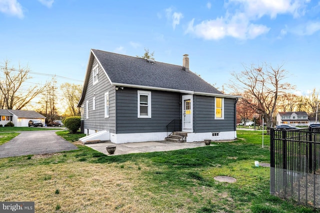 back of house featuring a chimney, a lawn, entry steps, fence, and a shingled roof