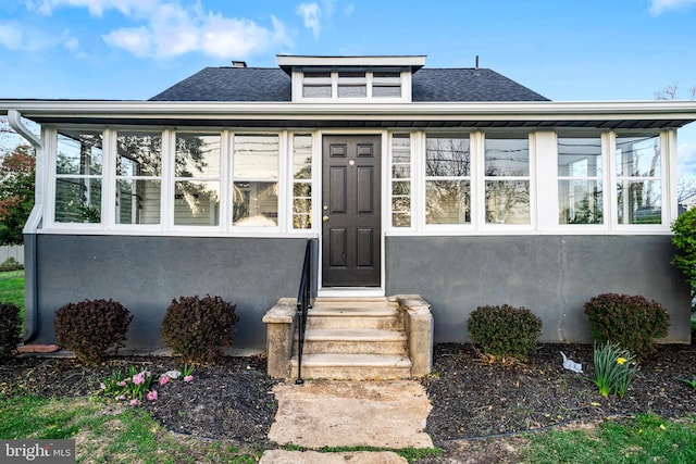 view of front of home featuring roof with shingles, entry steps, a sunroom, and stucco siding