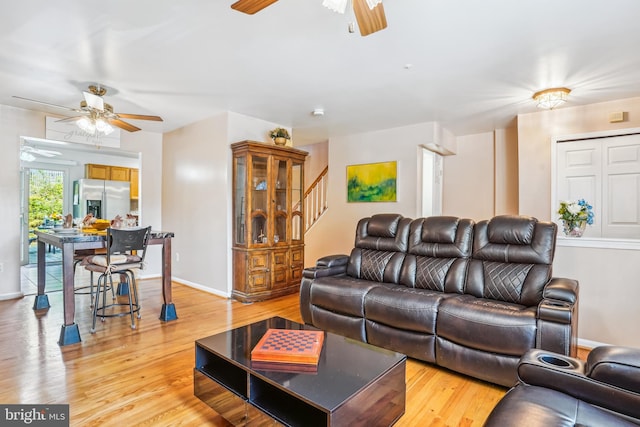 living area with a ceiling fan, light wood-style flooring, stairs, and baseboards