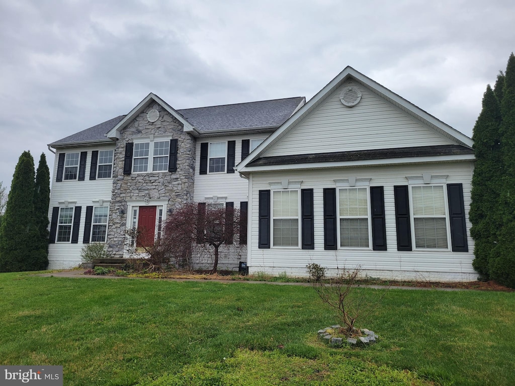 view of front of home featuring a front lawn, a shingled roof, and stone siding