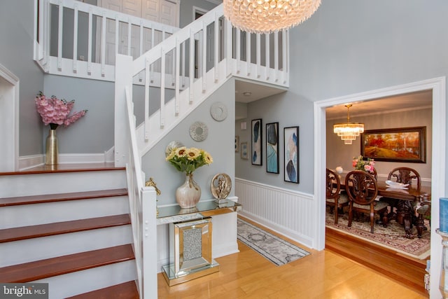 staircase featuring a chandelier, wood finished floors, a towering ceiling, and a wainscoted wall