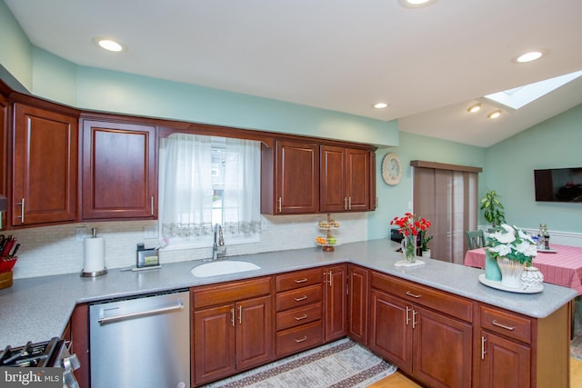 kitchen featuring a sink, appliances with stainless steel finishes, a peninsula, lofted ceiling with skylight, and decorative backsplash