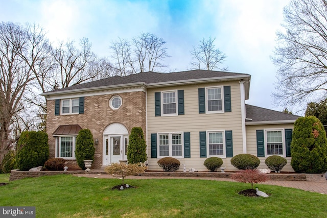 view of front of home featuring brick siding, a front yard, and roof with shingles