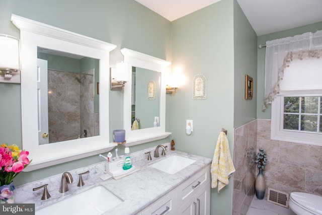full bathroom with toilet, double vanity, a sink, and visible vents