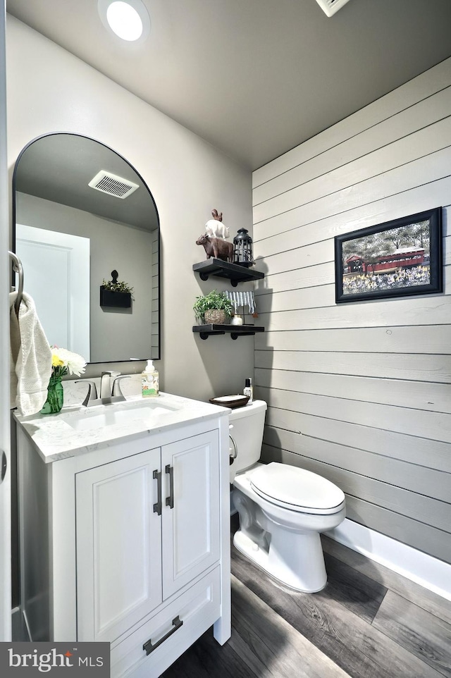 bathroom with vanity, wooden walls, toilet, visible vents, and wood finished floors