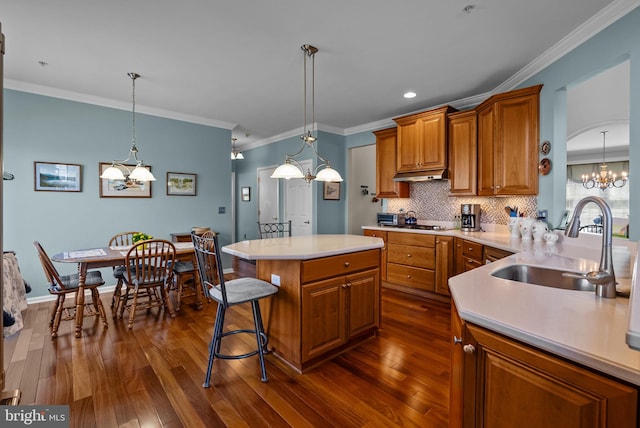 kitchen with under cabinet range hood, brown cabinetry, an inviting chandelier, a sink, and dark wood-style floors