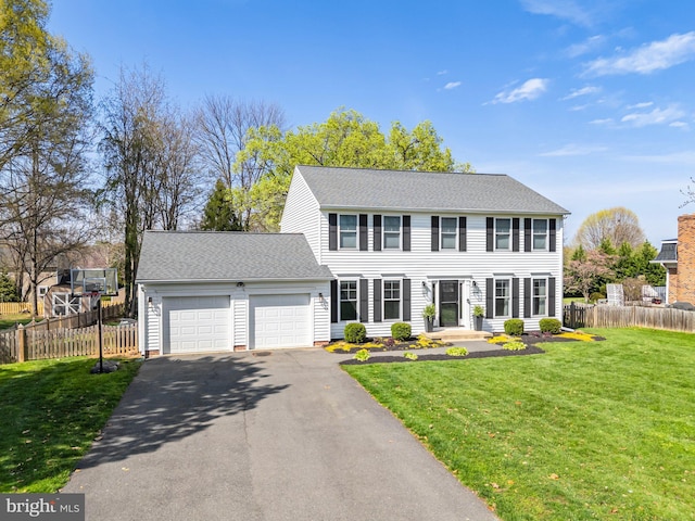 colonial-style house with aphalt driveway, a front yard, a garage, fence, and a shingled roof