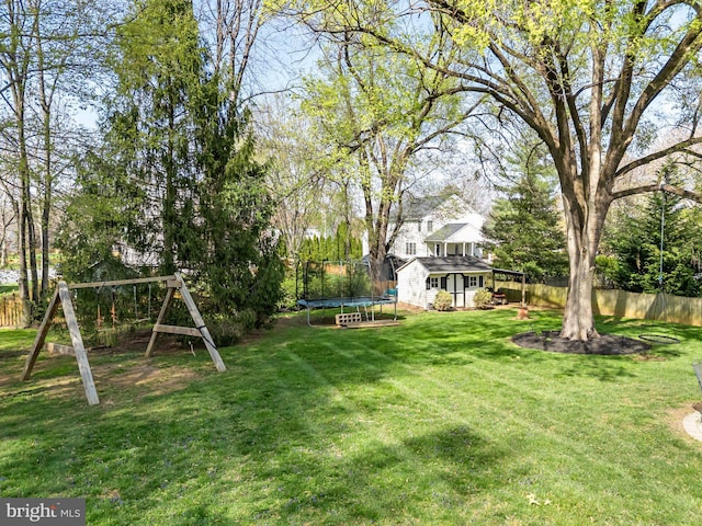 view of yard featuring a trampoline, fence, and an outbuilding