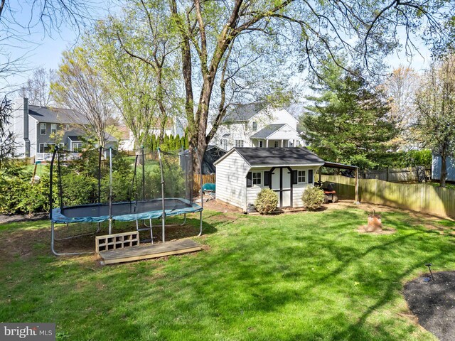view of yard featuring a trampoline, a fenced backyard, and an outdoor structure