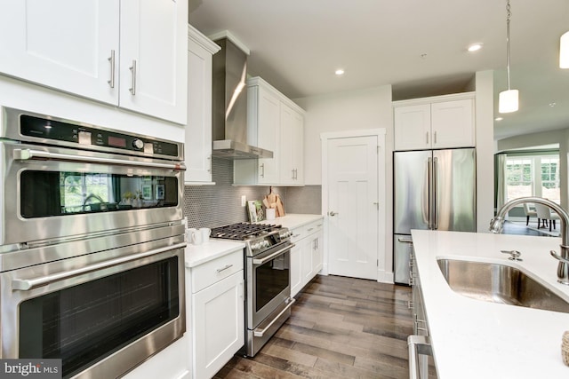 kitchen with a sink, wall chimney range hood, white cabinetry, stainless steel appliances, and backsplash