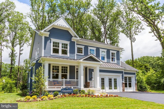 view of front of home featuring driveway, a front yard, a standing seam roof, metal roof, and covered porch
