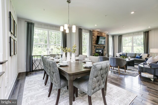 dining room with an inviting chandelier, a stone fireplace, hardwood / wood-style floors, and a healthy amount of sunlight