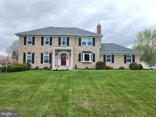 view of front of property with a front lawn, a chimney, and brick siding