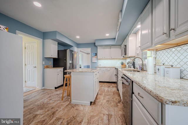 kitchen featuring white cabinets, a sink, a kitchen island, tasteful backsplash, and appliances with stainless steel finishes