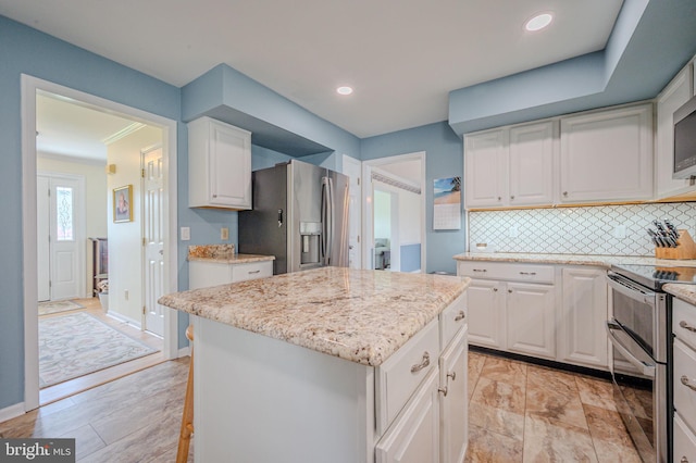 kitchen with decorative backsplash, white cabinetry, appliances with stainless steel finishes, light stone countertops, and a kitchen island
