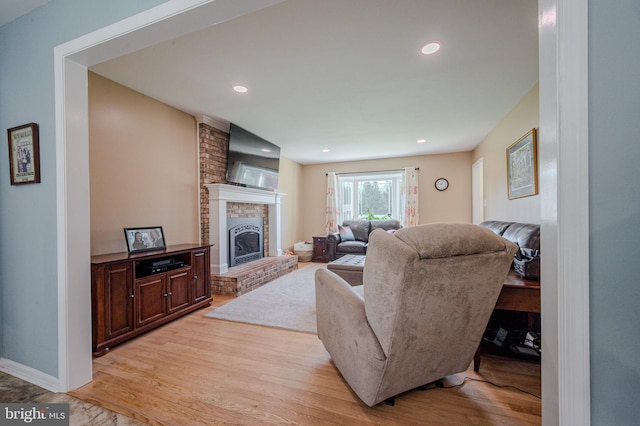 living room featuring recessed lighting, light wood-type flooring, and a brick fireplace