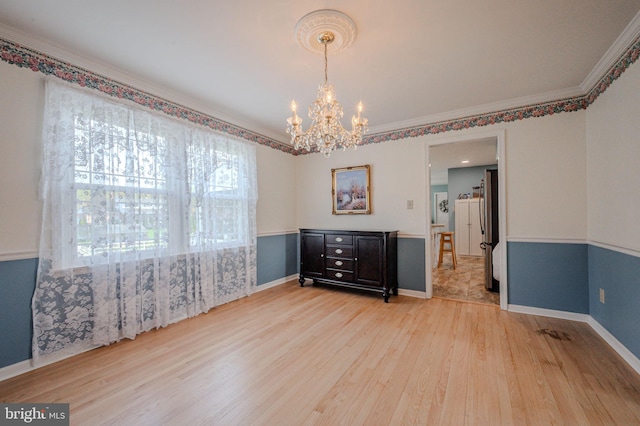 empty room featuring light wood-style flooring, crown molding, a notable chandelier, and plenty of natural light