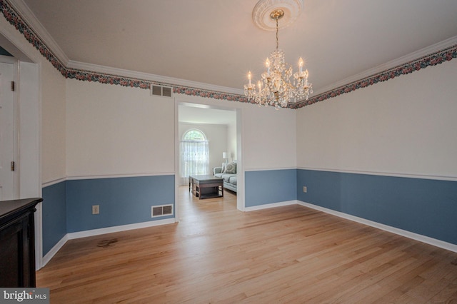 spare room featuring light wood-style flooring, visible vents, ornamental molding, and an inviting chandelier