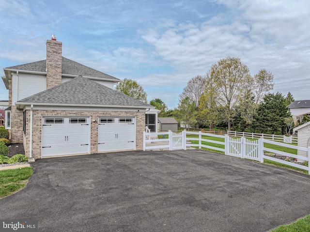 view of side of home featuring a chimney, aphalt driveway, fence, a shingled roof, and a garage