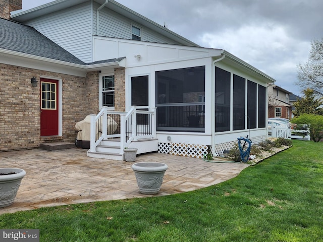 back of house with entry steps, a yard, roof with shingles, a patio, and a sunroom