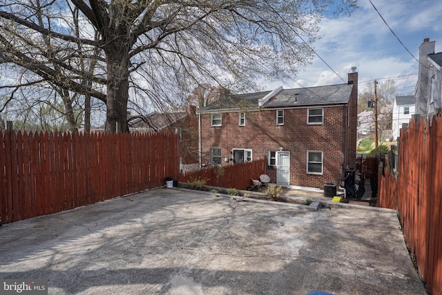 back of house featuring a patio, brick siding, fence, and a chimney