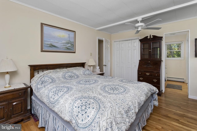 bedroom featuring crown molding, a baseboard heating unit, wood finished floors, and a closet