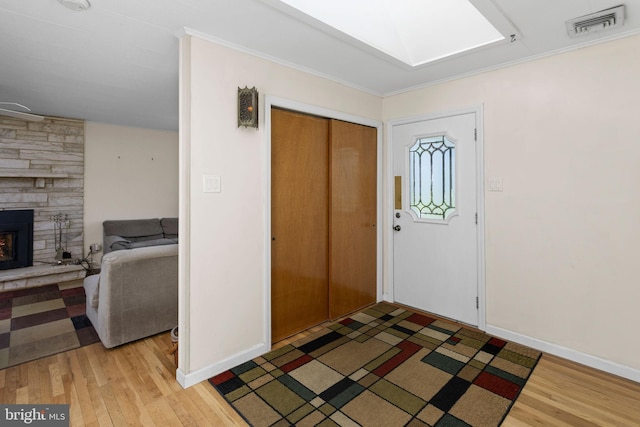 foyer entrance with baseboards, visible vents, a stone fireplace, and light wood-style floors