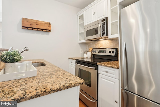 kitchen with a sink, glass insert cabinets, tasteful backsplash, white cabinets, and appliances with stainless steel finishes