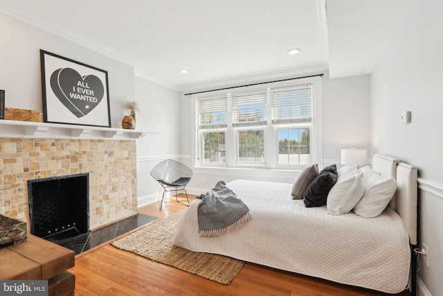 bedroom featuring a fireplace, wood finished floors, crown molding, and recessed lighting