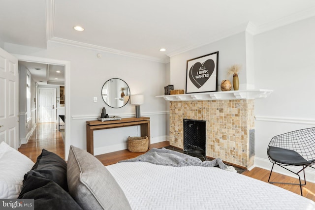 bedroom with baseboards, wood finished floors, a tile fireplace, and crown molding