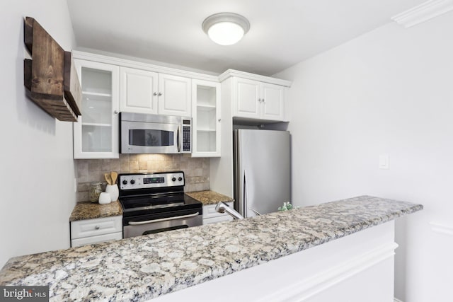kitchen with white cabinetry, decorative backsplash, glass insert cabinets, stainless steel appliances, and light stone countertops