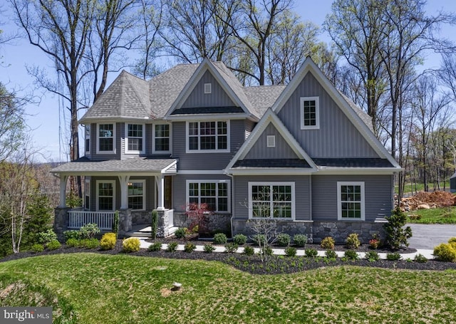 view of front facade with board and batten siding, covered porch, roof with shingles, a front yard, and stone siding