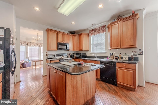 kitchen with a sink, light wood finished floors, black appliances, and a wealth of natural light