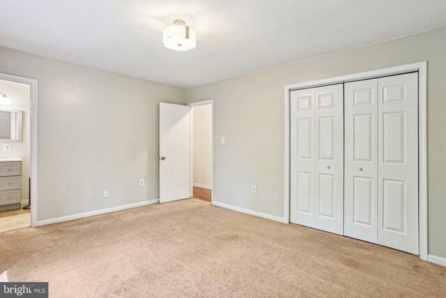 unfurnished bedroom featuring baseboards, a closet, light colored carpet, and ensuite bathroom